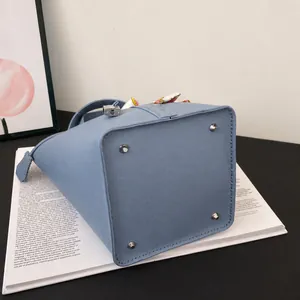 Detail view of light blue bucket bag with silver bottom studs and decorative scarf handle
