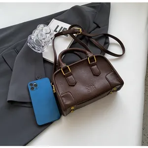 Detailed view of brown Boston bag with metal feet and adjustable strap on grey suit background