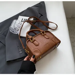 Close-up of brown textured leather Boston bag with gold studs and embossed logo