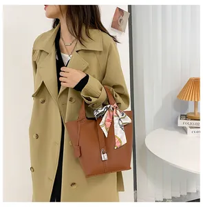 Braune Beuteltasche aus Leder mit rosa Seidentuch und silbernem Schloss am Trenchcoat