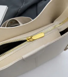 Detailed close-up of smooth light gold metal zipper on minimalist cream leather bucket bag