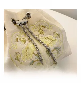 Dettaglio ravvicinato del ricamo floreale giallo e catena d'argento con perla sulla borsa