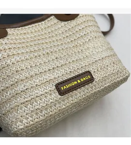 Gros plan du sac seau en paille tressé avec bordure en cuir brun et plaque de logo