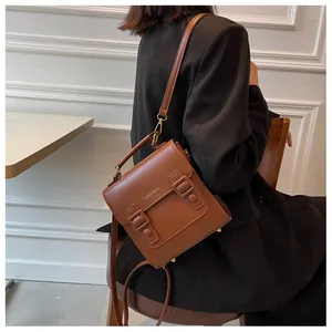 Brown vintage leather satchel with dual straps and gold buckles held by a model