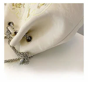 Dettaglio borsa a secchiello beige con ricami dorati e tracolla in perle chic