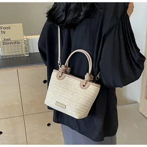 Détail du sac seau bicolore en paille avec bandoulière en cuir et plaque métallique