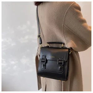 Close-up of black leather crossbody bag with dual buckles and golden logo on a beige coat