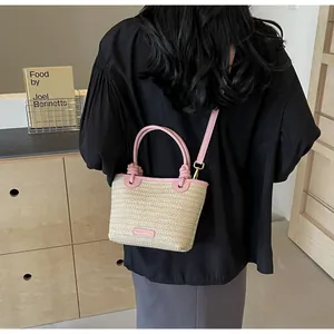 Vue détaillée d'un sac seau en paille avec bordure en cuir rose porté par un mannequin