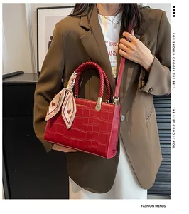 Detail of red crocodile pattern handbag with elegant pink silk scarf and gold hardware