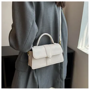 Détail du sac bandoulière beige minimaliste avec coutures en V sur un manteau habillé