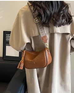 Brown lychee leather crossbody bag with colorful woven strap shown on a model