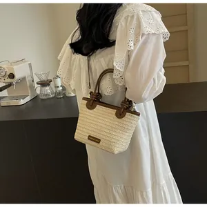 Détail du sac seau en paille avec poignées en cuir contrastées et étiquette logo