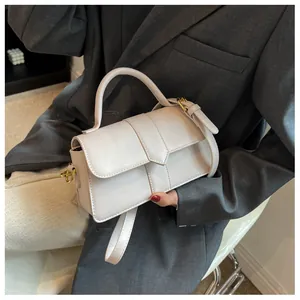 Détail du sac à main en cuir PU blanc cassé avec boucles dorées porté avec un tailleur gris