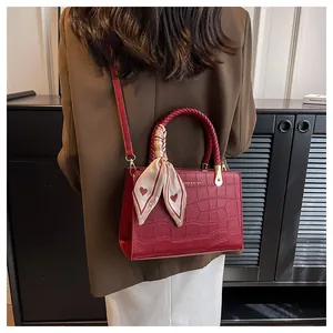 Detail of red crocodile texture handbag with woven handle and elegant silk scarf decoration
