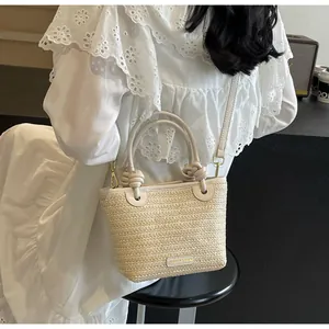 Détail du sac seau en paille avec bordure en cuir crème et poignée à nœuds élégante