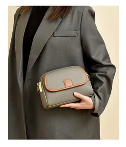 Close-up of grey litchi grain leather crossbody bag with brown trim detail and metal zipper