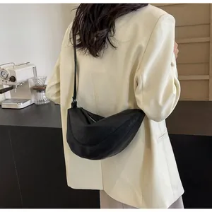 Detailopname van een zwarte halvemaanvormige schoudertas gedragen op een beige blazer