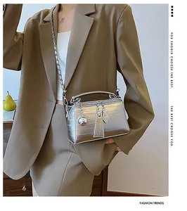 Detalle de bolso bandolera plateado en cuero grabado con cadena llevado por modelo