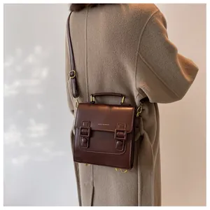 Brown vintage leather messenger bag with gold hardware worn over a camel wool coat