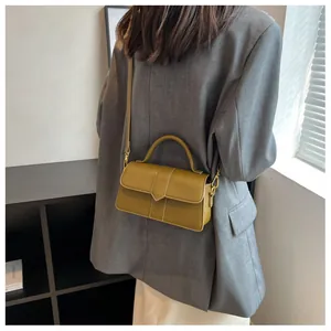 Sac bandoulière vert olive porté par un mannequin en blazer gris dans un décor moderne