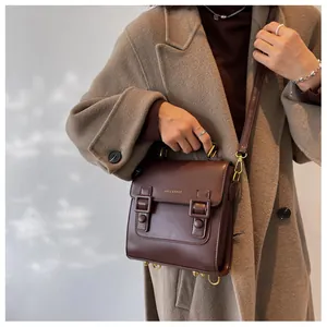 Detail of dark brown leather messenger bag with gold buckles and metallic brand logo