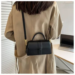 Détail du petit sac carré noir en cuir avec boucles dorées et poignée sur un manteau beige
