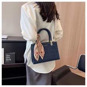 Detail of navy blue croc-embossed handbag with silk scarf on handle carried by model