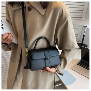 Sac bandoulière en cuir noir avec détails dorés porté sur un trench-coat élégant