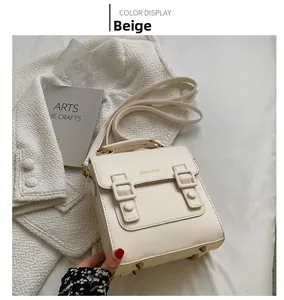 Detailed view of beige vintage crossbody bag with gold buckles on a textured fabric
