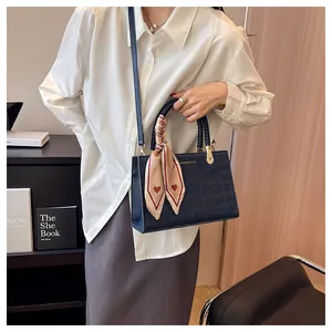 Detail view of navy faux crocodile handbag with silk scarf and gold brand lettering