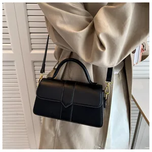 Détail du sac bandoulière noir minimaliste avec rabat en V et boucles dorées élégantes