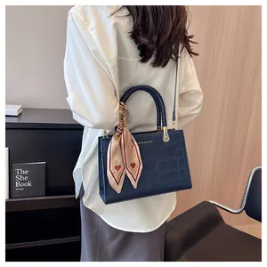 Detail of navy blue croc-effect handbag with woven handle and heart print silk scarf