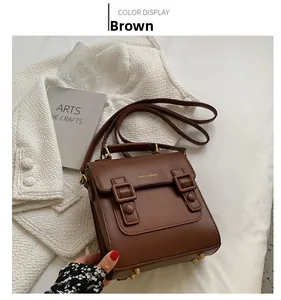 Brown vintage leather handbag with double buckle straps on elegant white tweed background