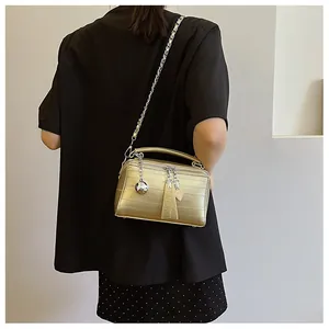 Modelo con bolso bandolera dorado metalizado con cadena de plata y colgante de bola