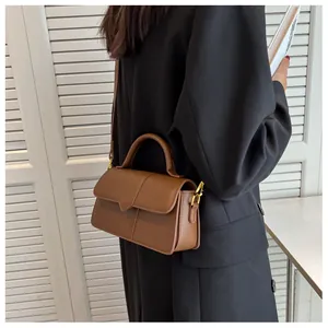 Gros plan du sac bandoulière en cuir marron avec rabat en V sur mannequin en costume