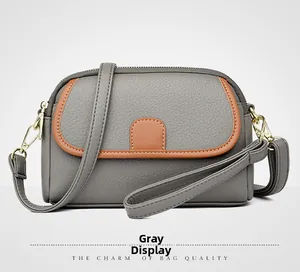 Detailed view of grey lychee textured crossbody bag with brown leather trim and gold hardware