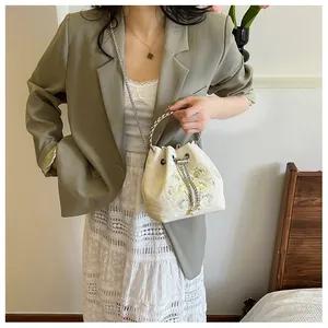 Ricamo dettagliato di fiori gialli su una borsa a secchiello in raso beige con catenella