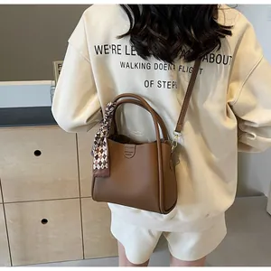 Brown lychee leather bucket bag with silk scarf on handle worn by casual model