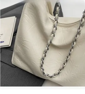 Close-up of pleated leather texture and silver chain strap on off-white crossbody bag