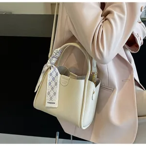 Detail of beige faux leather bucket bag with textured grain and decorative silk scarf