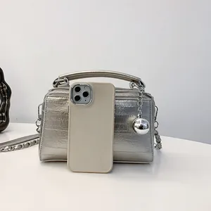 Bolso tipo caja plateado con cadena, asa de cuero y colgante de bola con móvil de escala