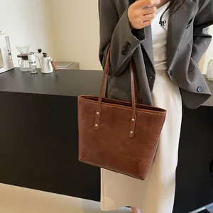 Brown geometric patchwork tote bag with long straps worn by a model in a cafe setting