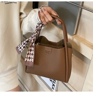 Brown textured leather tote bag with stylish scarf handle on a wooden bookshelf