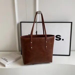 Brown large-capacity tote bag with geometric stitching and silver rivets on a display stand