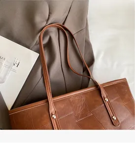 Close-up of the large brown patchwork tote bag with metallic rivet detail on the handle