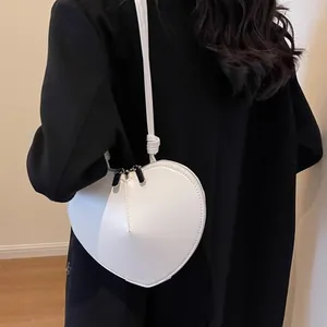 Bolso bandolera minimalista blanco con forma de corazón llevado con abrigo negro