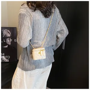 Detail of mini beige quilted crossbody bag with golden chain strap on a model
