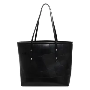 Large black tote bag with geometric leather patchwork design and silver rivet accents
