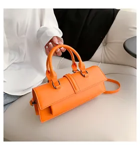 Detail der leuchtend orangefarbenen Umhängetasche mit runden Griffen auf einem Ledersofa