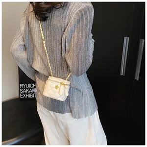 Detail of mini white quilted leather crossbody bag with golden camellia and chain strap